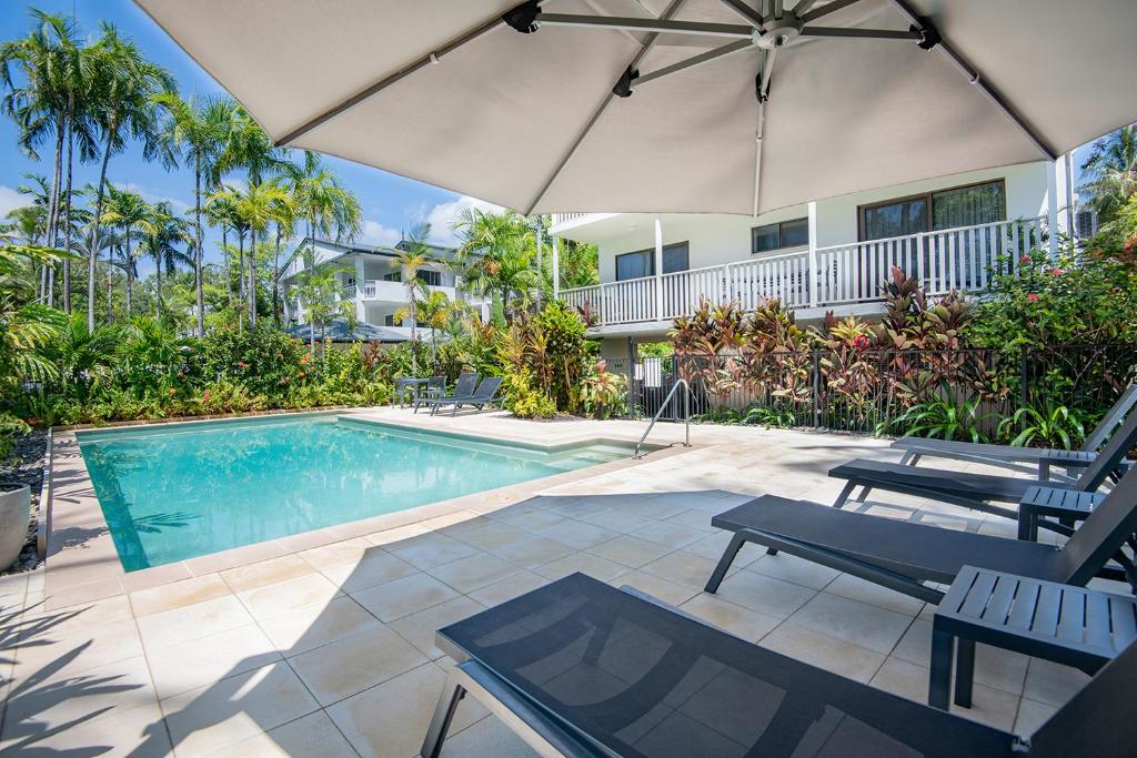 a swimming pool with an umbrella and two chairs at Unit 15 @ Tropical Reef: 2 mins to Four Mile Beach in Port Douglas