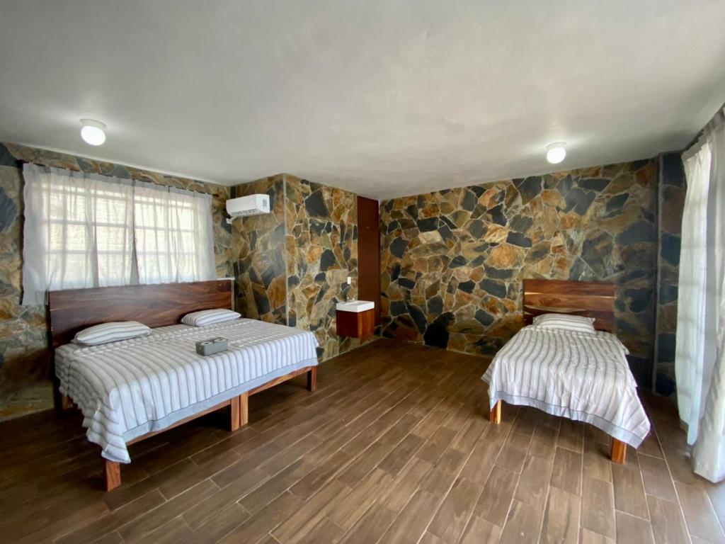2 Betten in einem Zimmer mit Steinwänden und Holzböden in der Unterkunft Sal Marina Restaurante y Cabañas in Salina Cruz