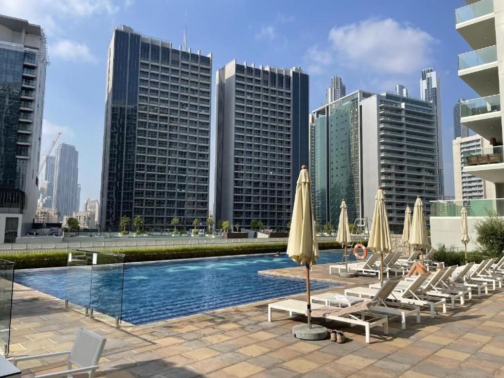 a pool with lounge chairs and umbrellas in front of buildings at Reva Residence Building, Step away from Dubai mall in Dubai