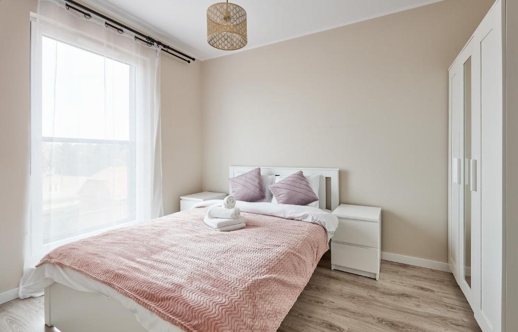 Dormitorio blanco con cama con manta rosa en Poznań Airport Homely Apartment, en Poznan