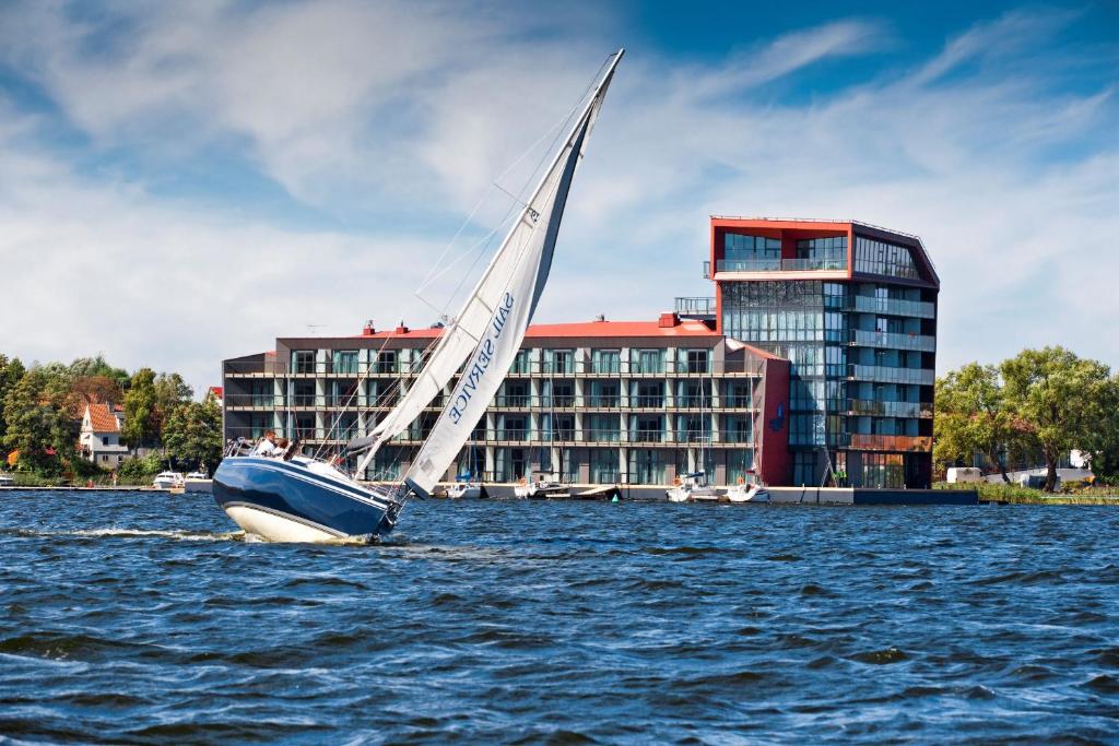 a sail boat in the water in front of a building at Hotel Mikołajki Leisure &amp; SPA - Destigo Hotels in Mikołajki
