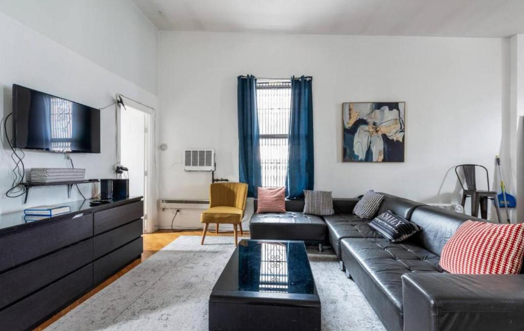 a living room with a black leather couch and a tv at Majestic 3 Bedroom Apartment in NYC! in New York