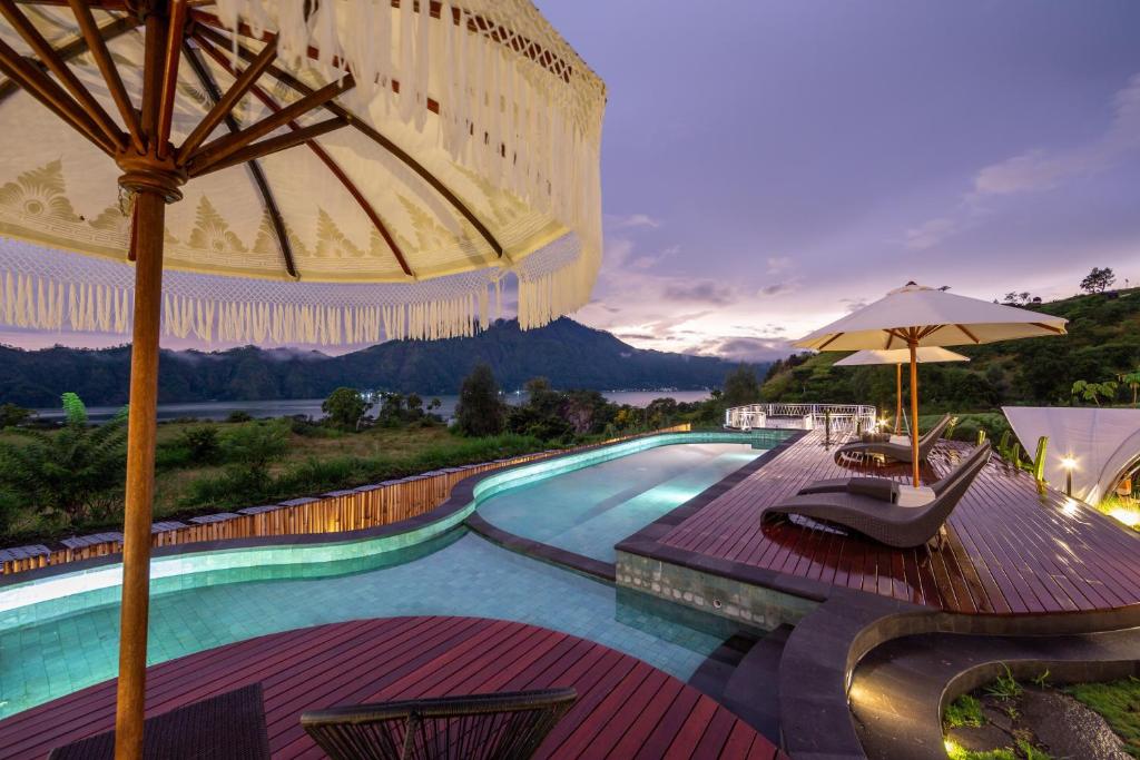 ein Resortpool mit Sonnenschirm und Stühlen in der Unterkunft The Dewi Kintamani Luxury Glamping and Natural Hotspring in Kintamani