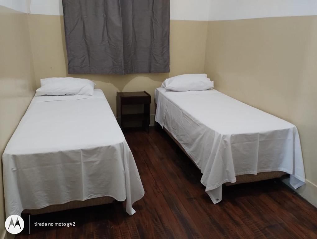 two beds in a room with white sheets at Hotel Central in Araçatuba