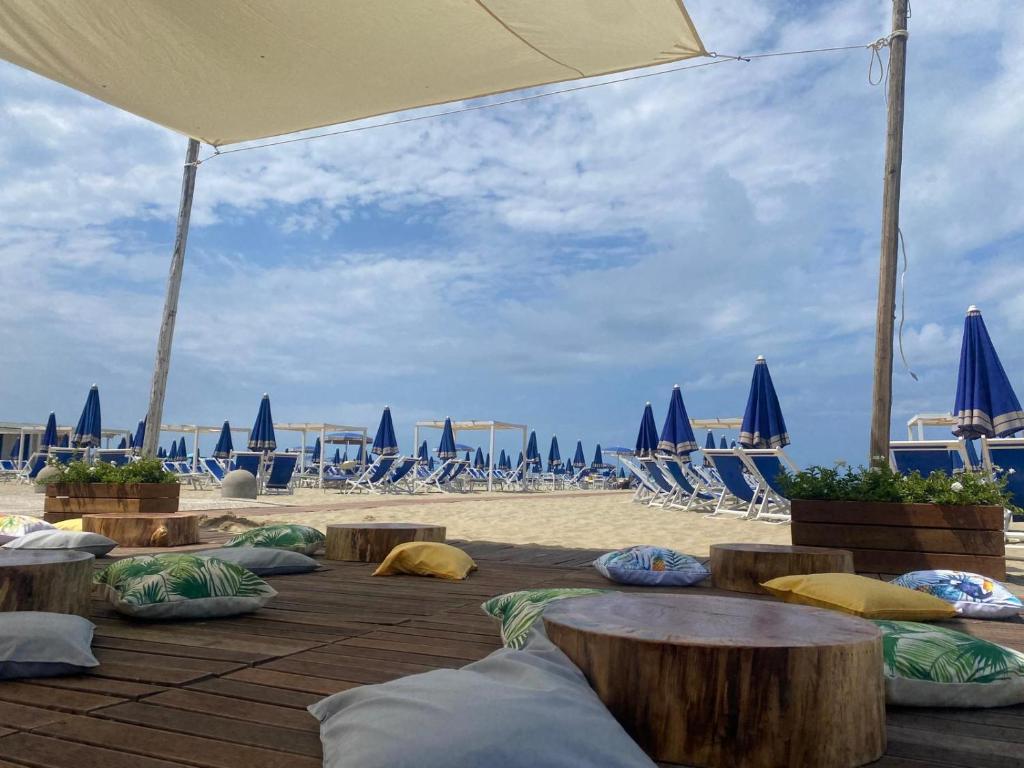 a beach with chairs and tables and blue umbrellas at Cosmopolitan Golf & Beach Resort in Tirrenia