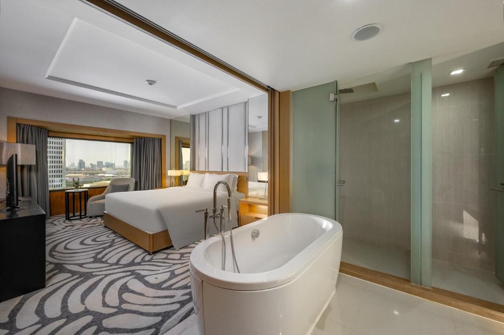 A bedroom bathroom with a freestanding soaking tub, glass shower and city view beyond.