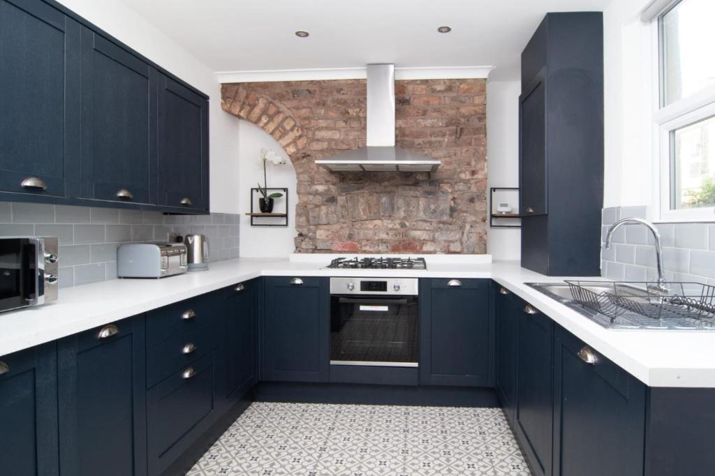 eine Küche mit blauen Schränken und einer Ziegelwand in der Unterkunft Central 4bed house, free parking in Liverpool