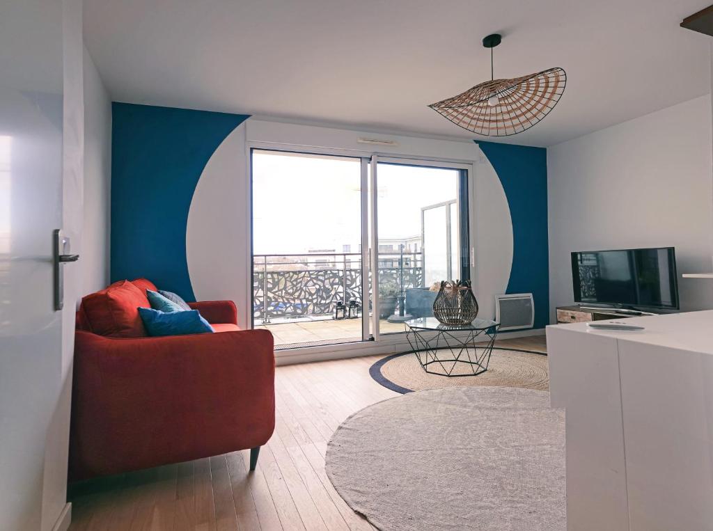 uma sala de estar com uma cadeira vermelha e uma grande janela em Appartement résidence neuve proche Versailles em Saint-Cyr-lʼÉcole