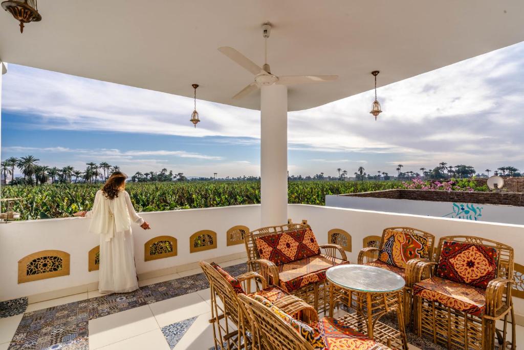 Eine Frau in einem weißen Kleid, die auf einer Veranda mit einem Tisch und Stühlen wandelt. in der Unterkunft Dar Lina Guesthouse Luxor in Luxor