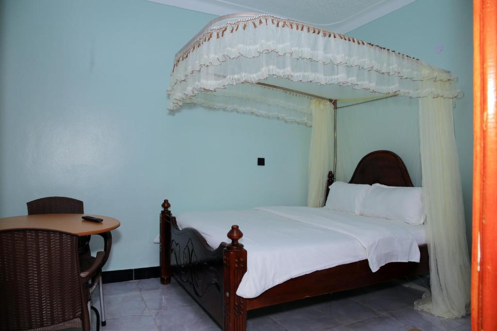 ein Schlafzimmer mit einem Himmelbett und einem Tisch in der Unterkunft JOSELLA MOTEL MUBENDE in Mubende