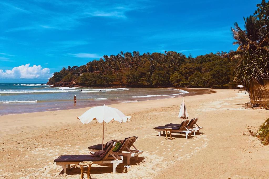 two lounge chairs and an umbrella on a beach at Calma - Surf, Yoga & Coffee on a Private Beach in Dickwella