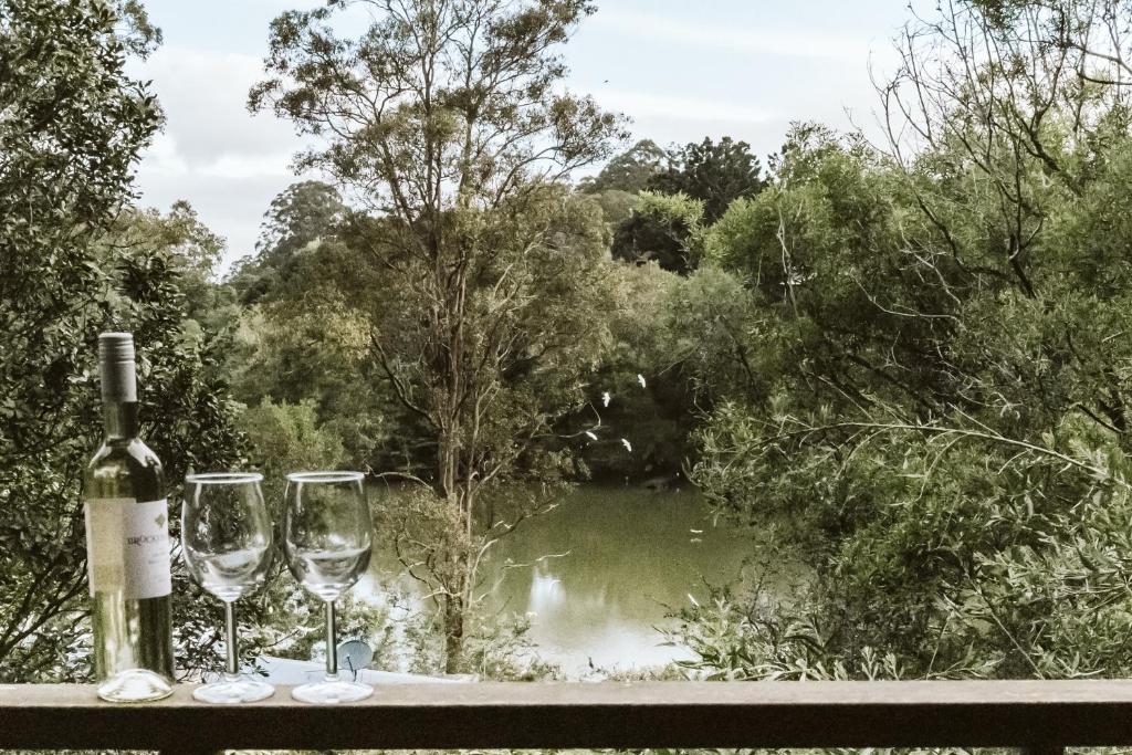 a bottle of wine and two glasses on a ledge with a pond at Kookaburra 2-Bedroom at On Burgum Pond Cottages in Maleny