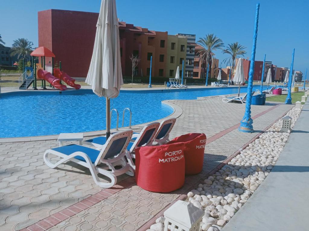 two chairs and an umbrella next to a swimming pool at شاليه ارضي 48 م بورتو مطروح in Marsa Matruh