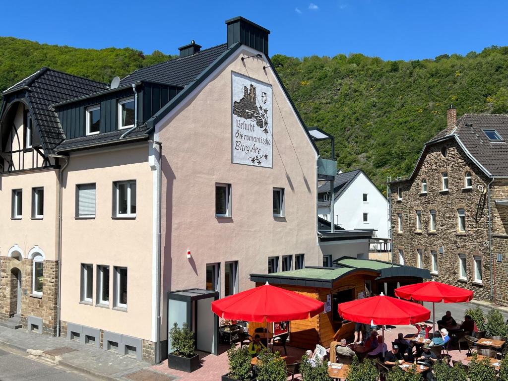 a building with tables and red umbrellas in front of it at Apart Hotel Lang in Altenahr
