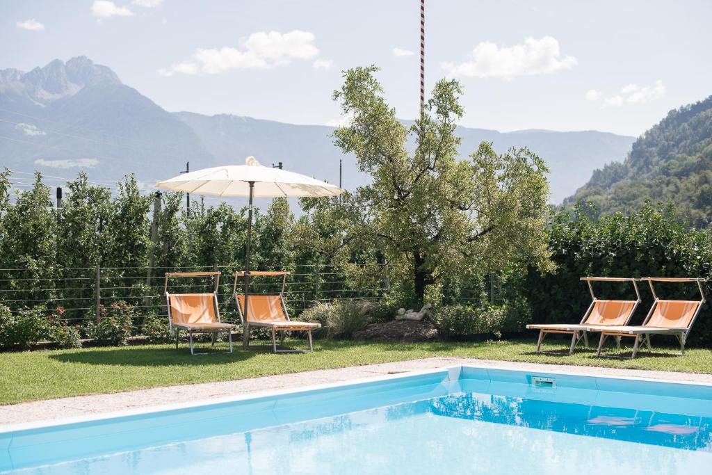 een zwembad met stoelen en een tafel en een parasol bij Untermairhof B&B Christine in Lagundo