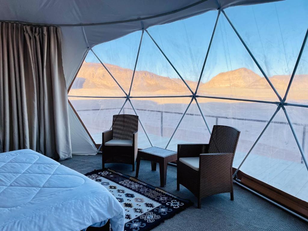 1 dormitorio con 1 cama, 2 sillas y una ventana grande en Shaheen Camp Wadi rum en Wadi Rum