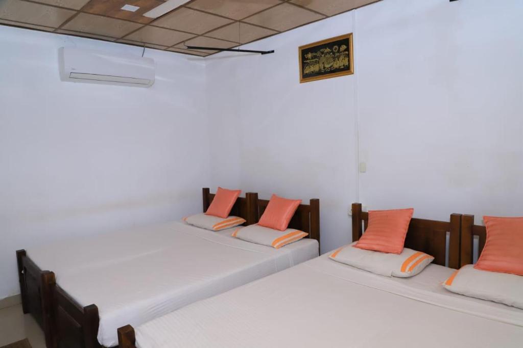 2 bedden in een kamer met witte muren en oranje kussens bij Dulmini Holiday Resort in Anuradhapura