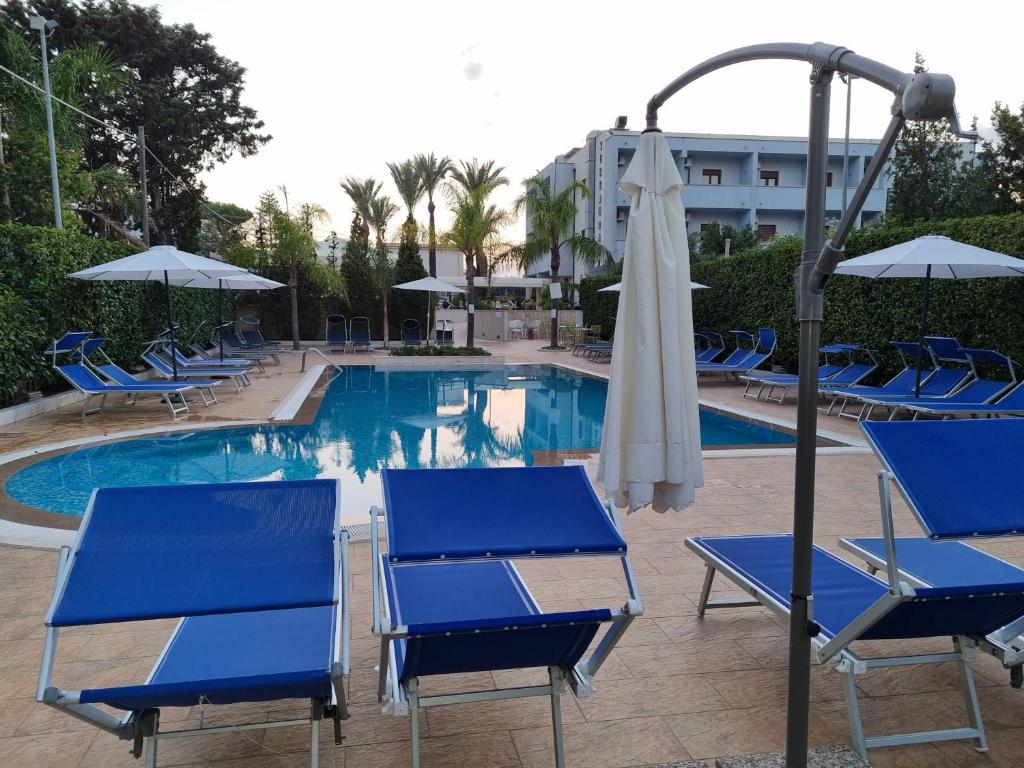 a group of blue chairs and an umbrella next to a pool at Hotel Costa Azul in Balestrate