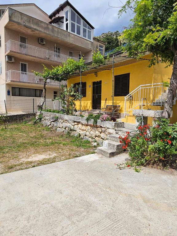 a yellow house with a stone wall in front of it at Apartman Ljubo in Podgora