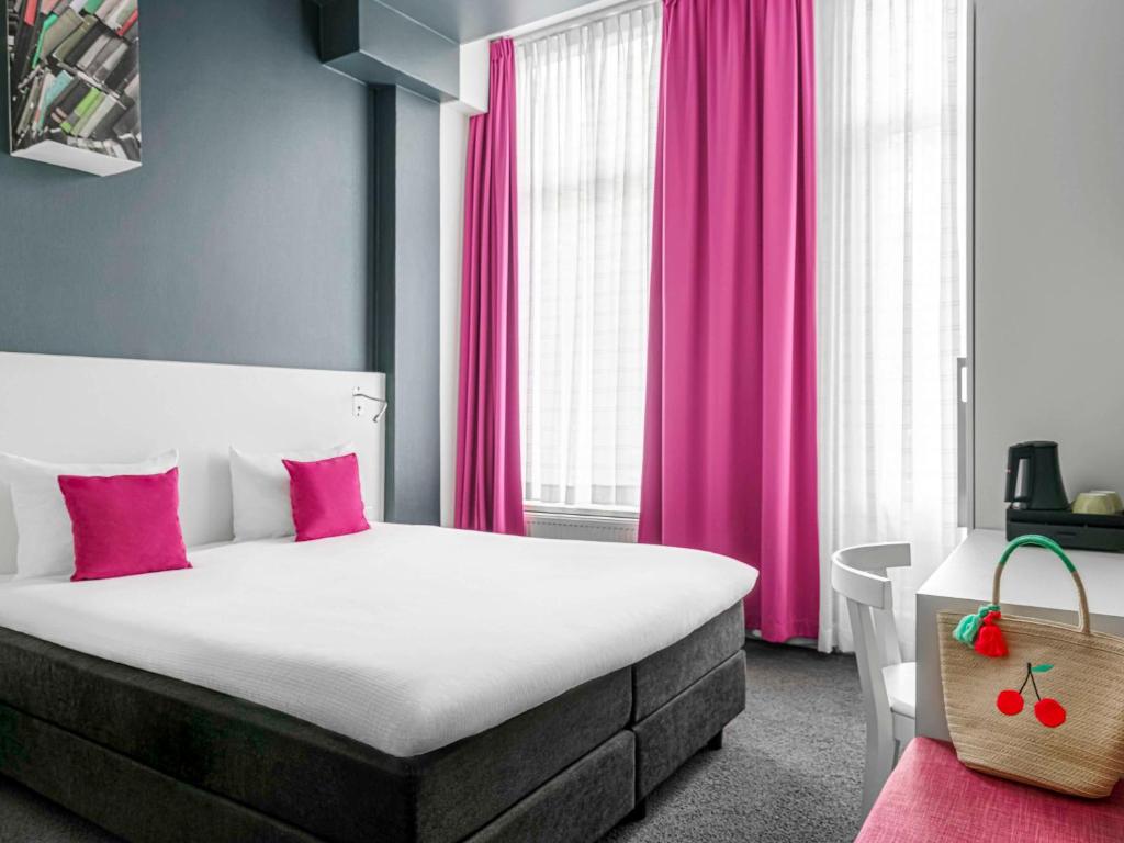 a bedroom with a large bed with pink curtains at ibis Styles Amsterdam Amstel in Amsterdam