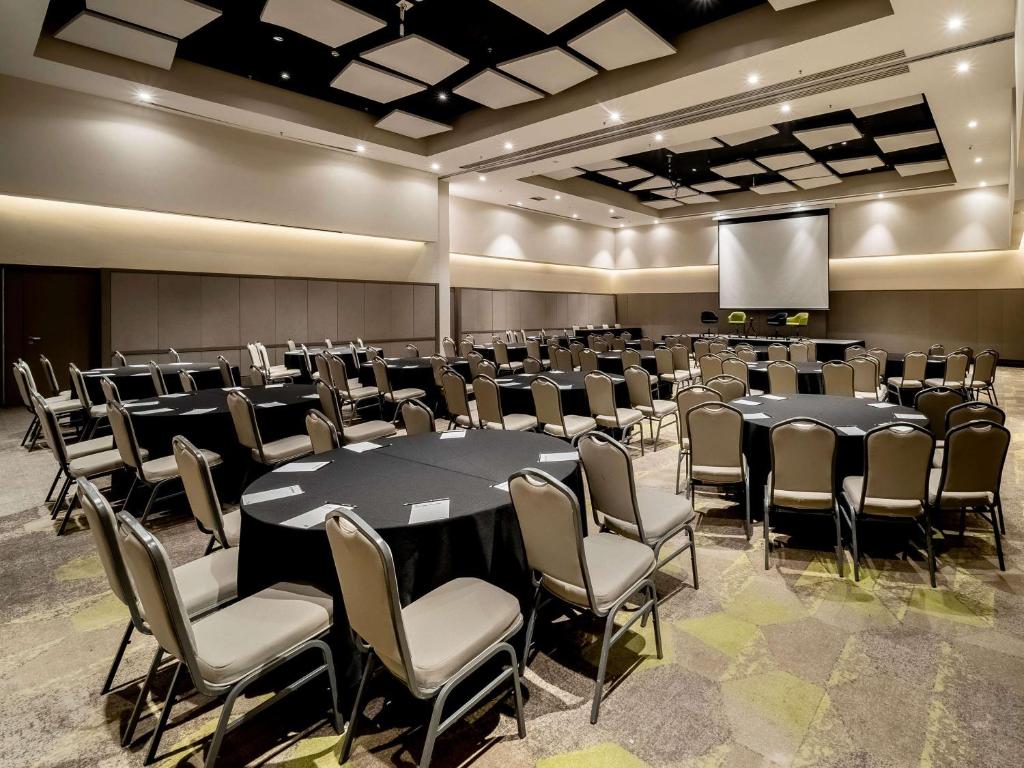 a conference room with tables and chairs and a screen at Pullman Sao Paulo Guarulhos Airport in Guarulhos
