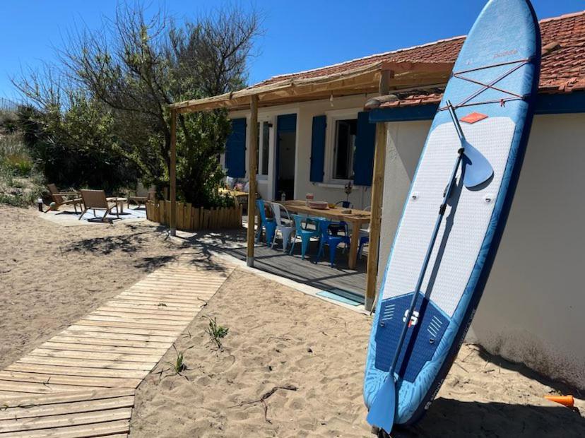 une planche de surf bleue est appuyée contre une maison dans l'établissement Cabanon bohème les pieds dans le sable et en première ligne de mer, à Marseillan