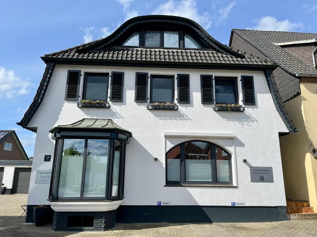 une maison blanche avec un toit noir et des fenêtres dans l'établissement Ferienwohnung am Glockensee, à Bad Laer