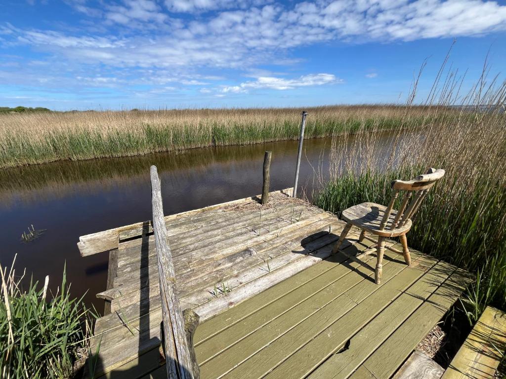 een houten dock met een stoel op het water bij Bilberghus - Beyond Bed and Breakfast in Bjerregård