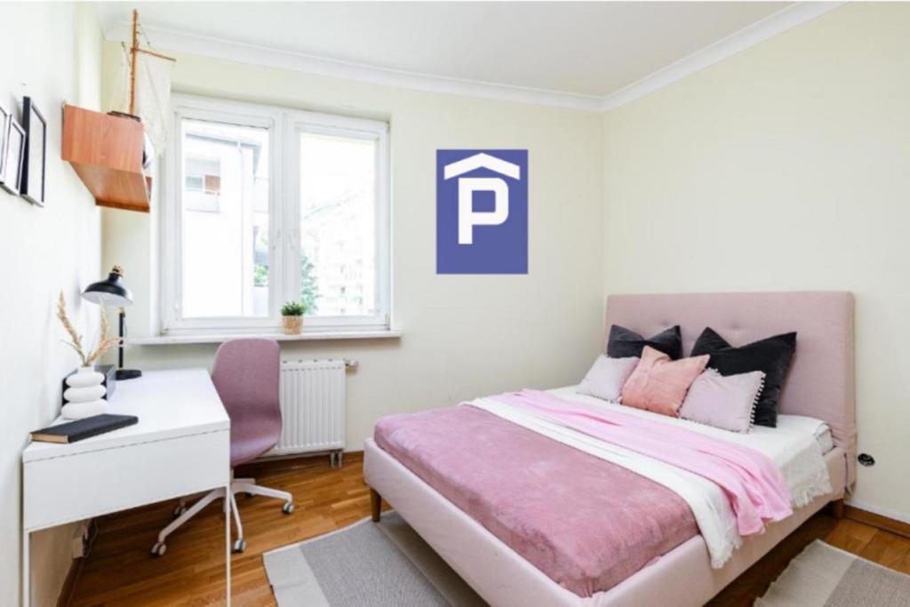 Habitación blanca con cama rosa y escritorio. en SuperApart Relaksowa 37 en Varsovia