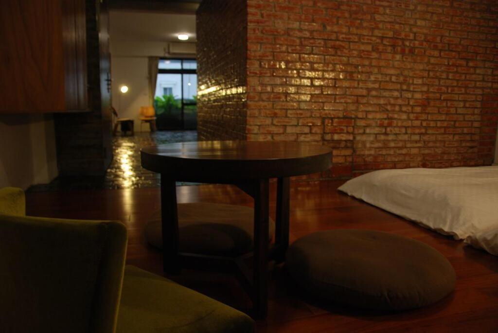 a room with a table and a bed and a brick wall at Howcome spots homestay in Hualien City