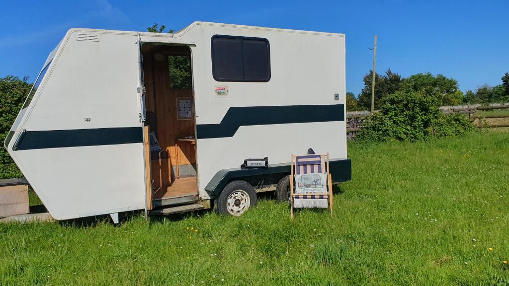 a white trailer with a chair in a field at Trailor Escape GLAMPING POD - our converted horse box at Nelson Park Riding Centre - Birchington, Margte, Thanet, Ramsgate, Broadstairs, Sandwich, Herne Bay in Birchington
