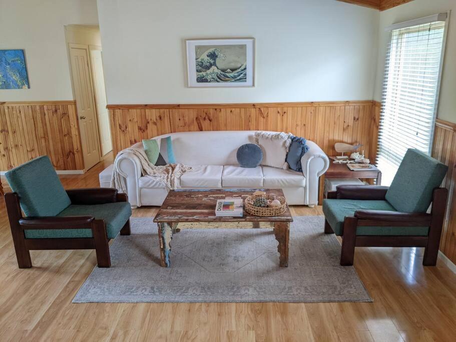 a living room with a white couch and two chairs at beach house in Venus Bay