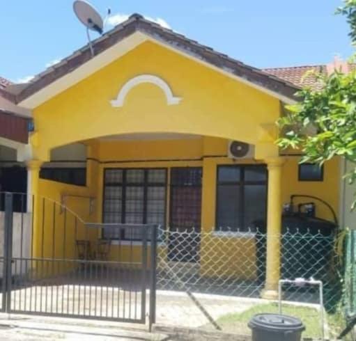 une maison jaune avec une clôture devant elle dans l'établissement Sobey Laris Homestay QASEH, à Pasir Mas