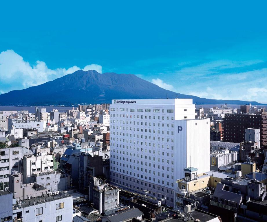 a large white building with a mountain in the background at Sun Days Kagoshima in Kagoshima
