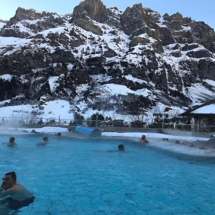 um grupo de pessoas em uma piscina com uma montanha coberta de neve em mountain bliss & hot springs em Leukerbad
