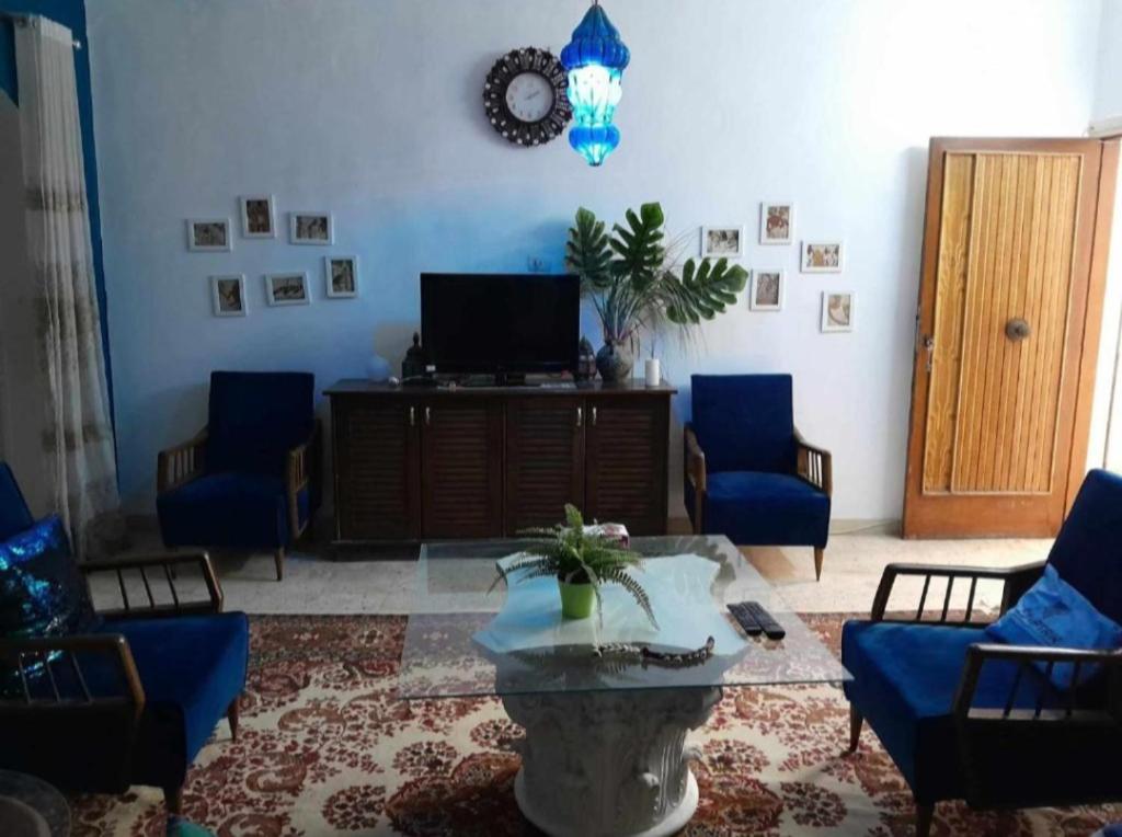 sala de estar con sillas azules, mesa y TV en La Casa pyramids Inn en El Cairo