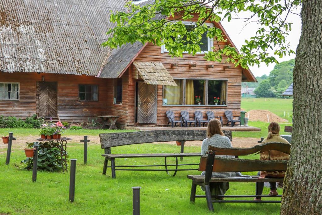 two women sitting on a bench in front of a house at Lauku viesu māja Bajāri in Rucava