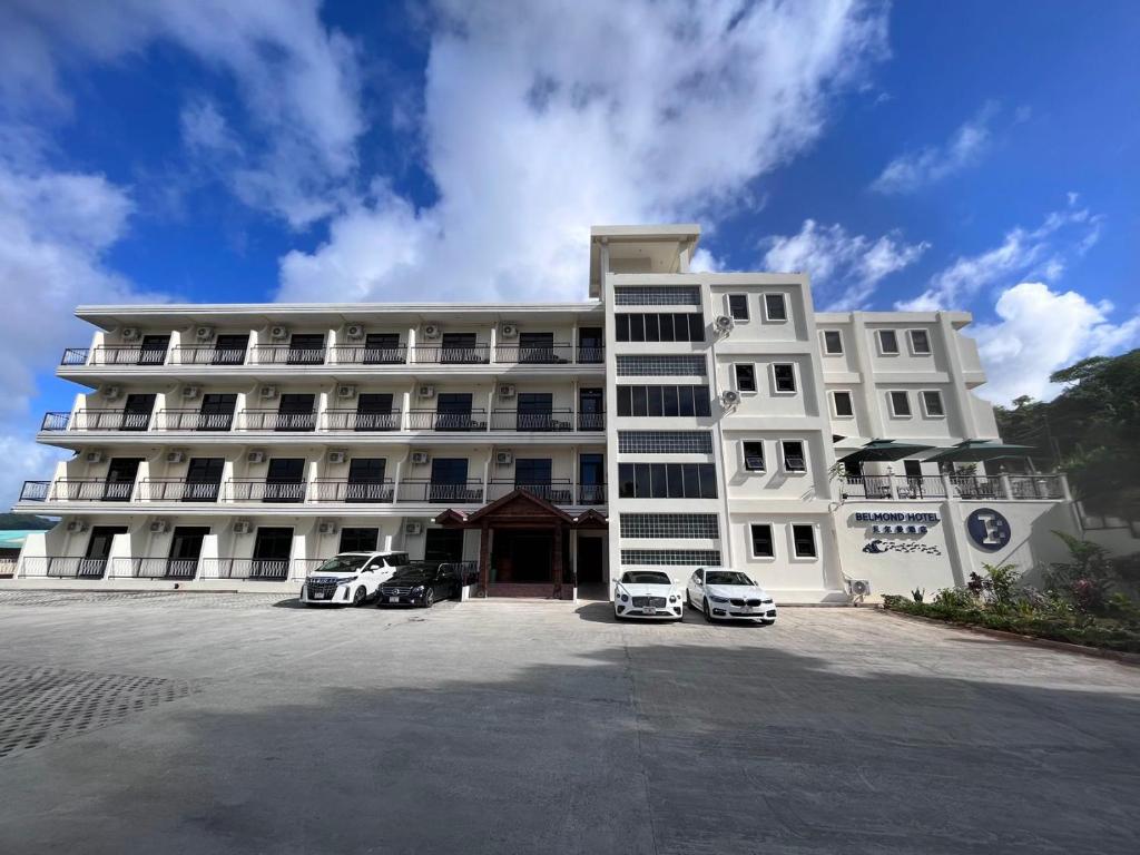 a large white building with cars parked in front of it at Belmond Hotel 贝尔曼酒店 in Koror