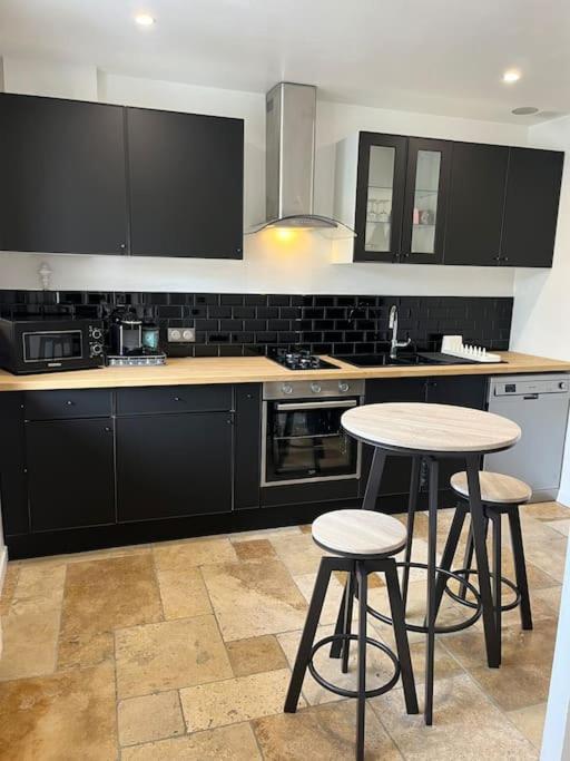 une cuisine avec des placards noirs et deux tabourets de bar dans l'établissement La p tite maison, à Gien