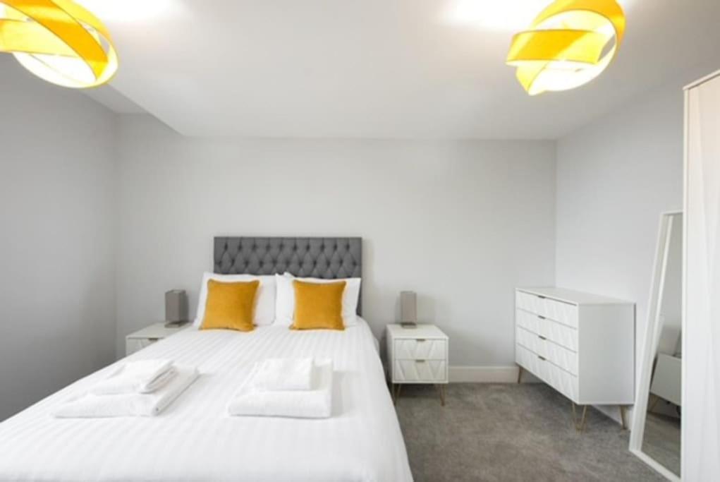 a white bedroom with a large bed with yellow pillows at Cosy, Bright and Spacious Flat in Brentwood