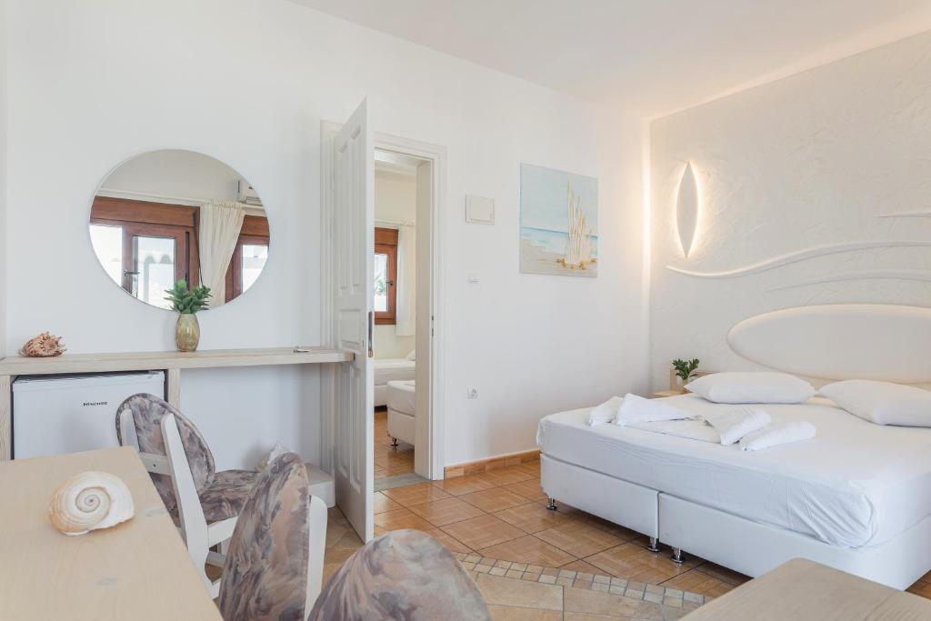 a white bedroom with a bed and a mirror at Kokkari Beach Hotel in Kokkari