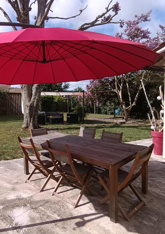 une table et des chaises en bois avec un parapluie rouge dans l'établissement Charmante maison landaise, à Soustons