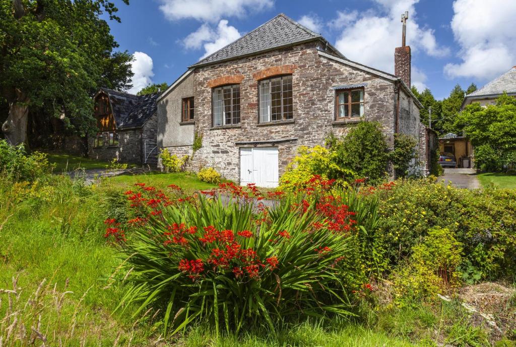 uma velha casa de pedra com flores no quintal em Barn Cottage, Brayford em Charles