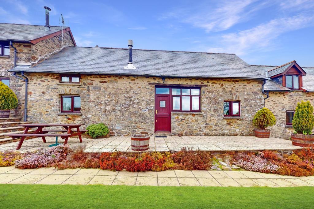 una casa de piedra con una puerta roja y un banco en Kiri Cottage Hawkridge, en Dulverton