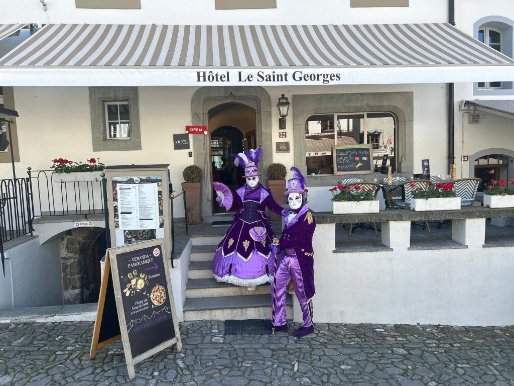 dwoje ludzi ubranych w kostiumy stojących przed budynkiem w obiekcie Le Saint Georges w mieście Gruyères