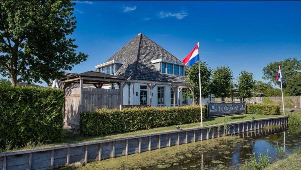 een huis met een vlag en een bord naast een rivier bij Cozy chalet near Amsterdam at Camping Venhop in Berkhout