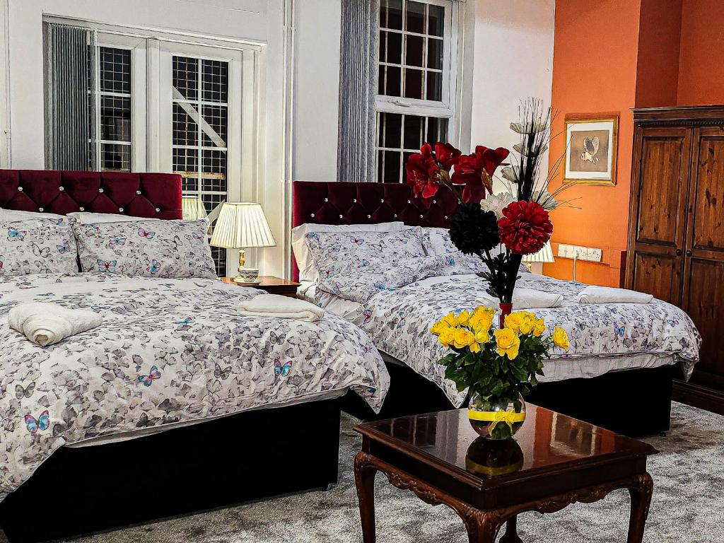 un dormitorio con 2 camas y una mesa con un jarrón de flores en The Trinity Lodge - Self Serviced en West Bromwich