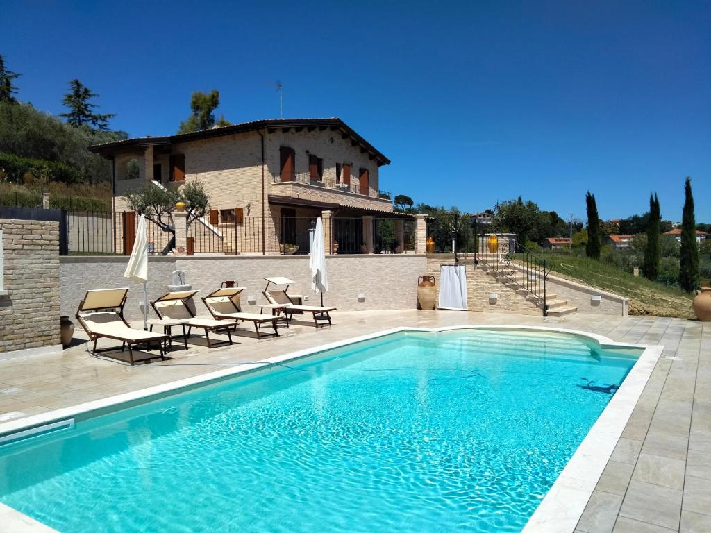 a swimming pool with chairs and a house in the background at B&B L' Antica Fonte in Spinetoli