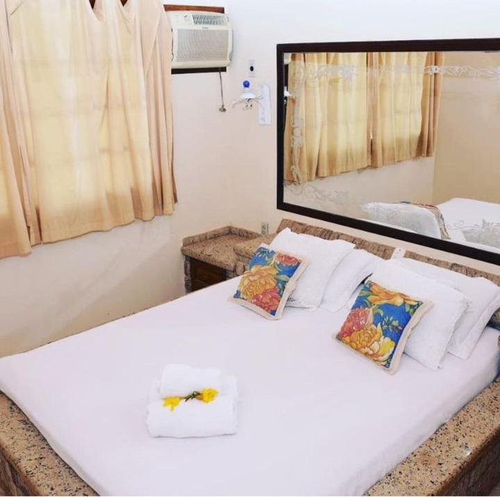 ein weißes Bett mit zwei Kissen und einem Spiegel in der Unterkunft Pousada Recanto Das Palmeiras in Búzios