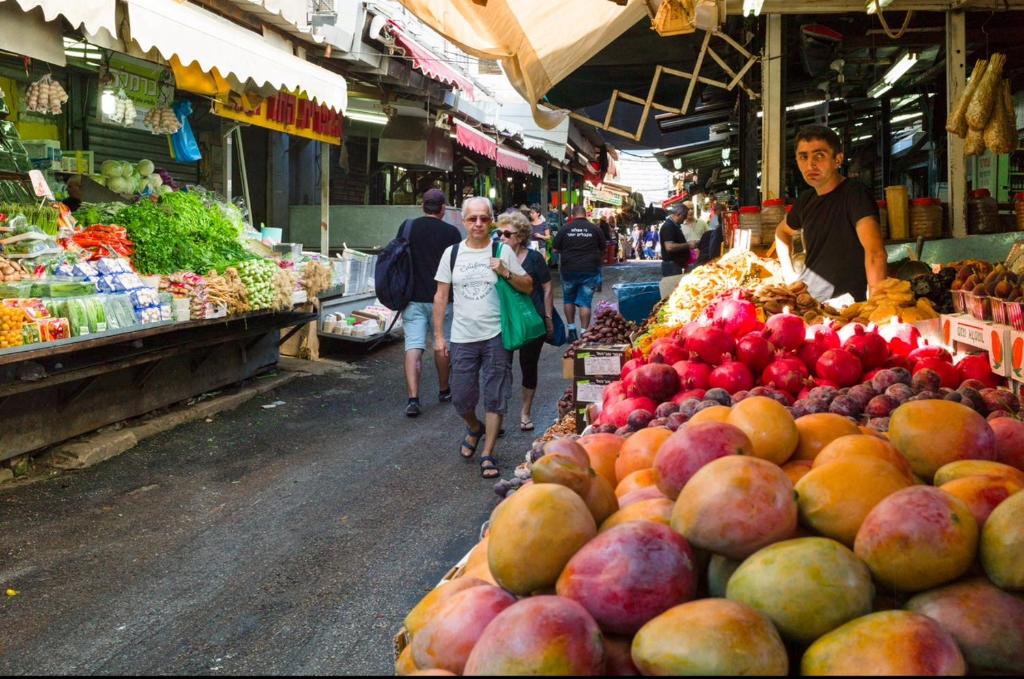 a group of people walking through a market with fruits and vegetables at Carmel Market center apartments TLV in Tel Aviv